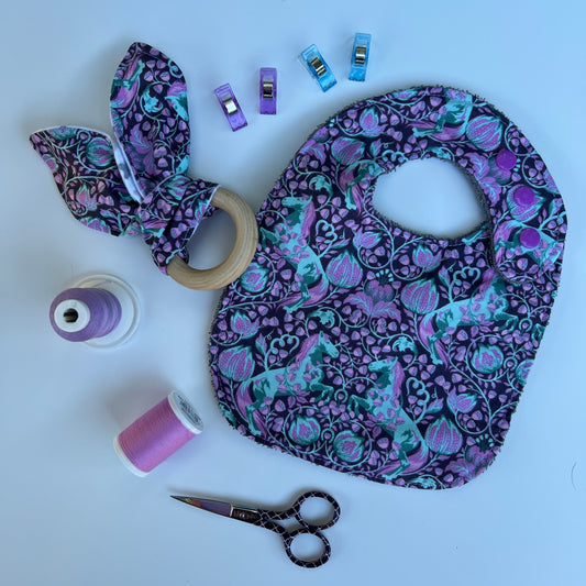 Baby bib, teether, and sewing supplies on a white background