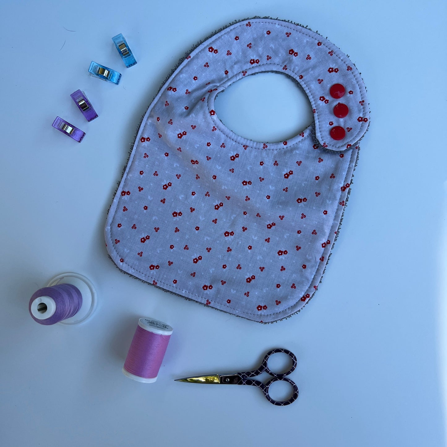 Gray bib with red sequins, scissors, and spools of thread on a light blue background