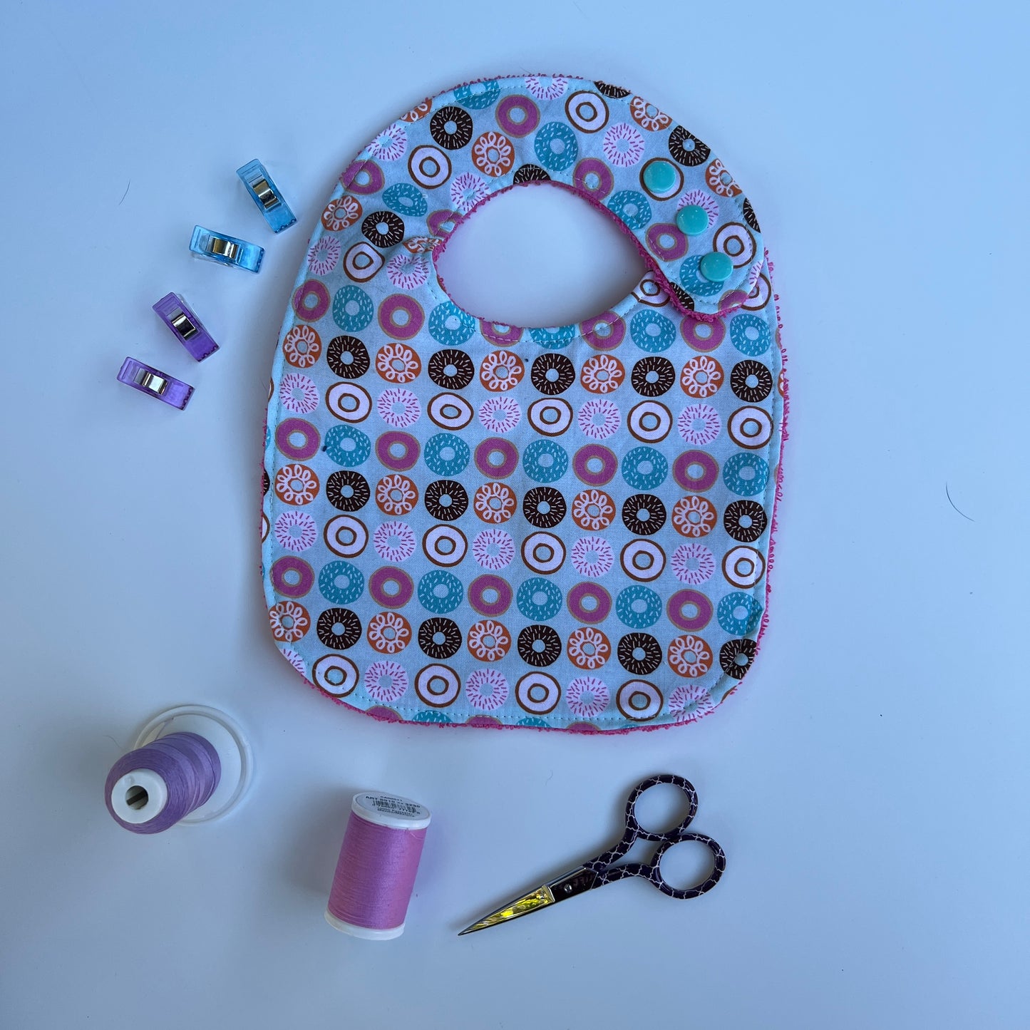 Floral-patterned baby bib with sewing supplies on a light blue background
