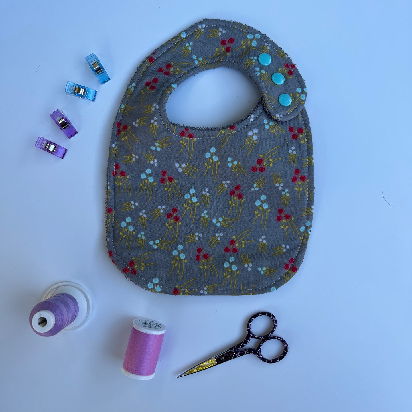 Fabric bib with floral pattern on a white background with sewing supplies.