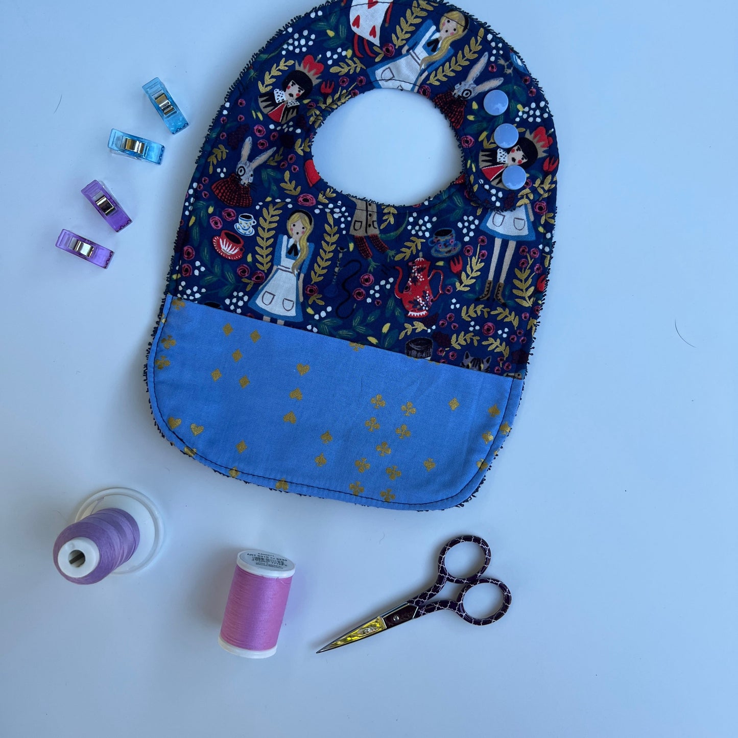 Fabric  with blue and patterned design, scissors, and spools of thread on a white background